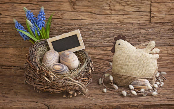 A charming HD desktop wallpaper of an Easter nest with eggs, a small chalkboard, blue flowers, and a fabric chicken on a rustic wooden background.