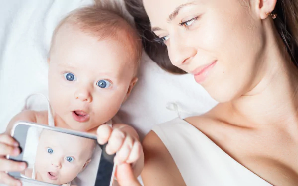 Smiling mother and blue-eyed baby holding a phone showing the baby's face; bright close-up photography, 5K Ultra HD PC desktop wallpaper/background.