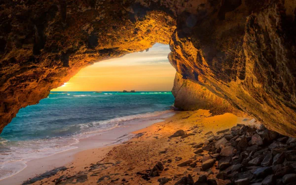 A stunning view of a cave arch overlooking a blue sea and horizon at sunset, showcasing the beauty of nature with golden hues illuminating the rocky shoreline.