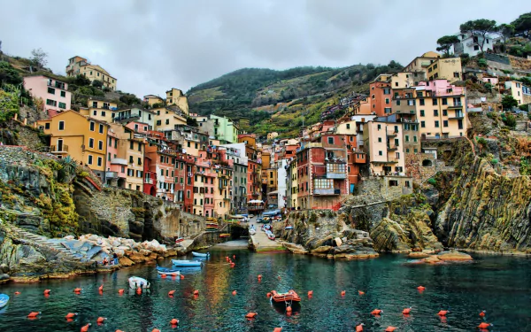 A picturesque view of Riomaggiore in Cinque Terre, Italy, featuring colorful houses lining a rocky coastline, with boats floating in the calm water below a misty sky.