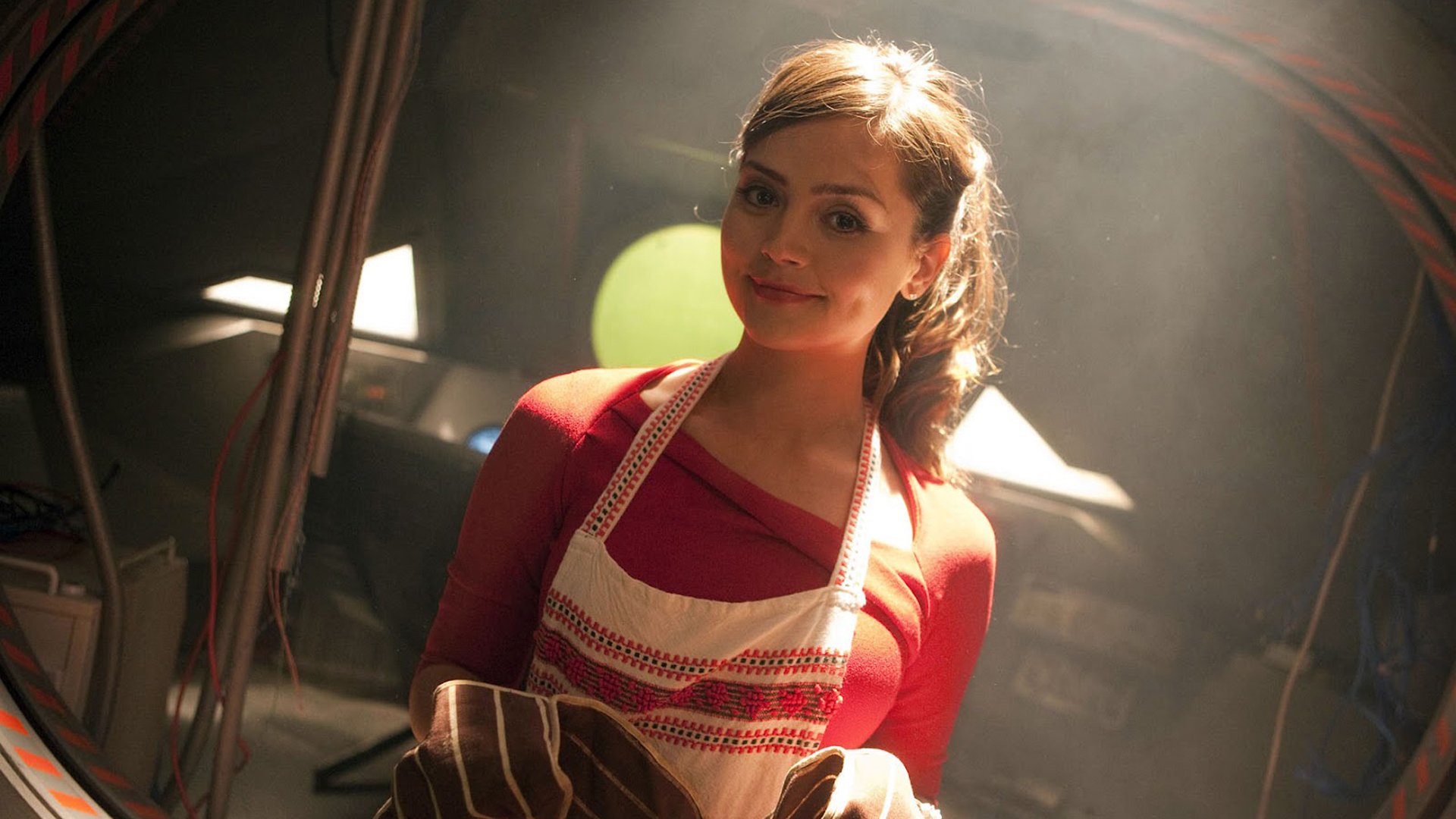 HD PC desktop wallpaper of Clara Oswald from the TV show Doctor Who (2005), smiling in an apron amid warm, atmospheric lighting.