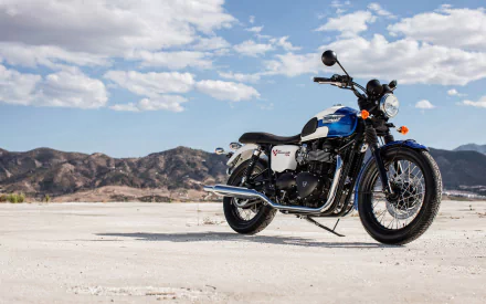 HD PC desktop wallpaper: blue-and-white Triumph Bonneville motorcycle vehicle parked on a sunlit salt flat with distant mountains under a bright, partly cloudy sky.
