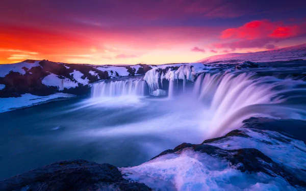 Goðafoss waterfall in Iceland flows amid ice at sunset, showcasing vibrant skies and serene natural beauty in this HD desktop wallpaper.