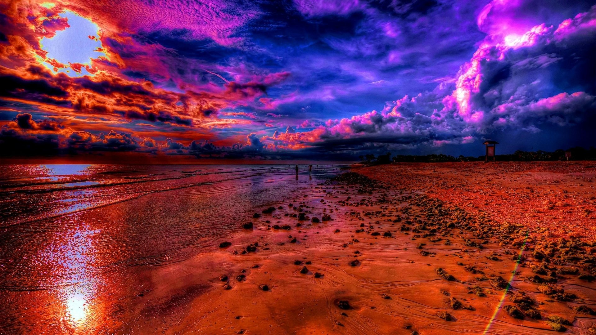 Vivid HDR photograph of a sunset over an ocean horizon, depicting a colorful sky and a beach dotted with rocks. HD desktop wallpaper and background.