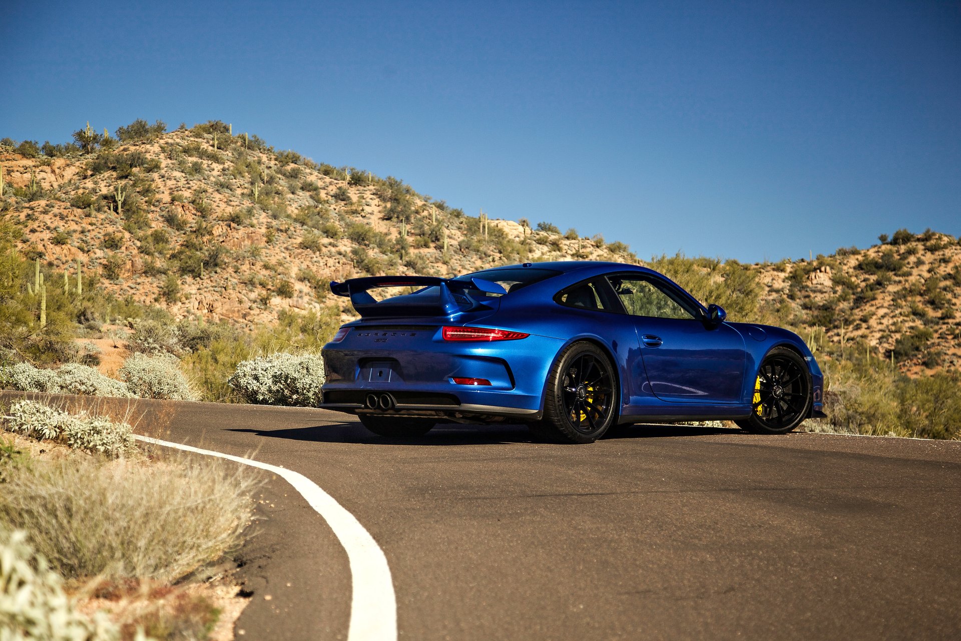 Blue Porsche 911 GT3 parked on a winding desert road under a clear blue sky, captured in 4K Ultra HD for PC desktop wallpaper and background.