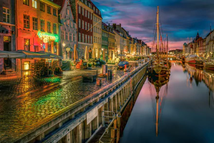 A vibrant evening scene in Copenhagen, with colorful buildings lining a calm canal, reflecting on the water. A boat is docked, capturing the essence of the town's charm.