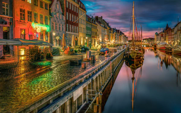 A vibrant evening scene in Copenhagen, with colorful buildings lining a calm canal, reflecting on the water. A boat is docked, capturing the essence of the town's charm.
