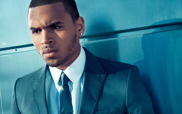 A stylish Chris Brown in a sharp suit, captured with intense expression against a blue background, making a striking HD desktop wallpaper for music fans.
