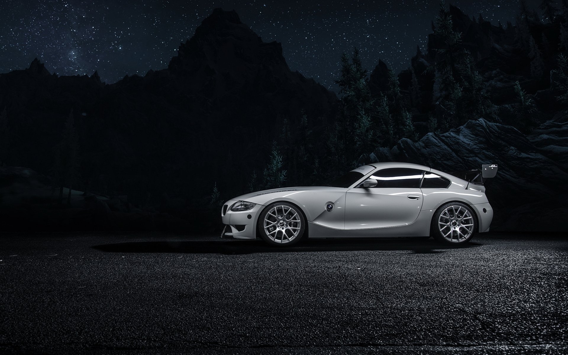 A white BMW Z4 sports car is parked on a dark road at night, framed by silhouetted mountains under a starry sky in this HD desktop wallpaper.