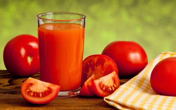 A glass of vibrant red tomato juice surrounded by fresh whole and sliced tomatoes on a wooden surface with a yellow checkered cloth, captured in 8K Ultra HD.