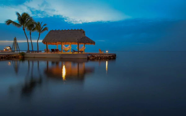 A tranquil tropical scene at dusk, featuring a thatched bungalow beside the calm ocean, with palm trees, a hammock, and gentle reflections, creating a serene holiday atmosphere.