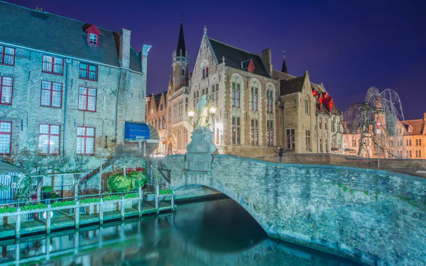 Nighttime cityscape of Bruges, Belgium, featuring historic buildings and a stone bridge over calm water, captured in HD for a stunning desktop wallpaper.