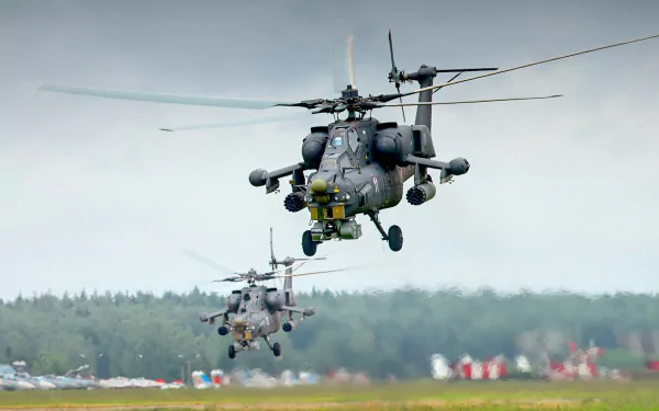 HD desktop wallpaper featuring two Mil Mi-28 military helicopters flying low over a runway with a cloudy sky and forest in the background.