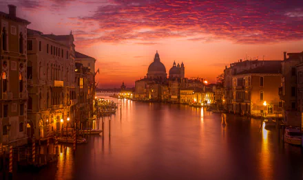A stunning view of the Grand Canal in Venice at night, illuminated by golden lights under a colorful sky, showcasing the city's iconic architecture and tranquil waters.