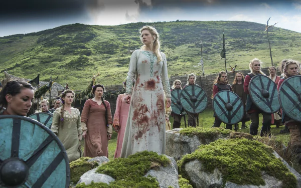 Image of Lagertha, portrayed by Katheryn Winnick, standing amidst a group of warriors in a dramatic scene from the TV show Vikings, featuring a landscape of green hills.