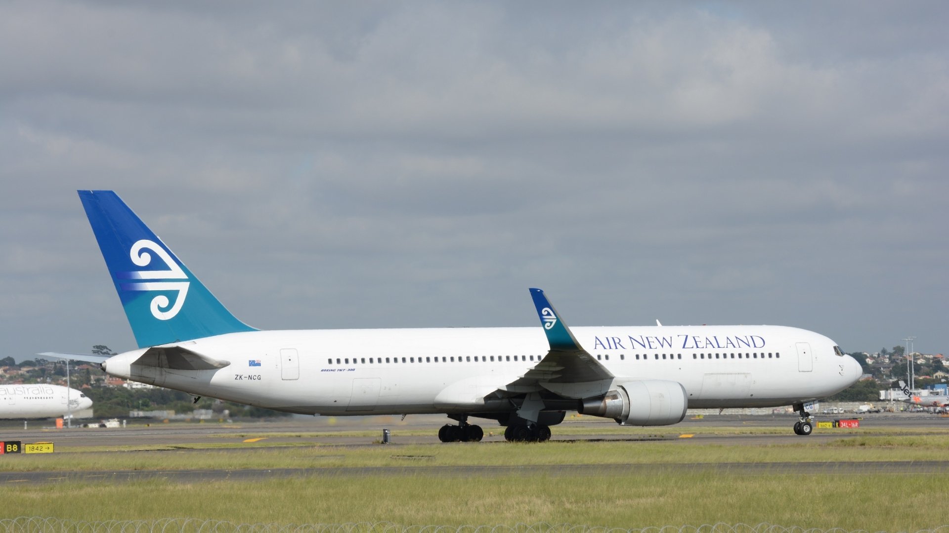 HD desktop wallpaper of a Boeing 767 passenger plane from Air New Zealand, showcasing the aircraft on a runway under a cloudy sky.