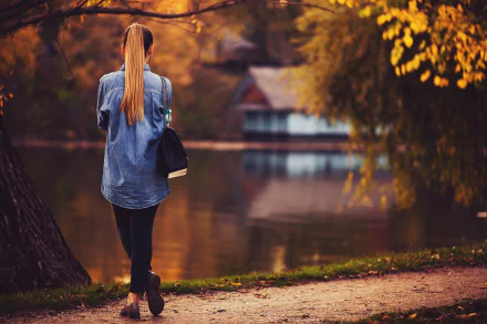 A woman with long hair walks near a lake surrounded by autumn foliage, creating a serene fall scene in this HD desktop wallpaper.
