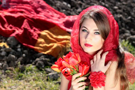 A woman with long hair and blue eyes poses elegantly, wearing a red scarf and lipstick, holding a bouquet of vibrant tulips, against a backdrop of rich colors.