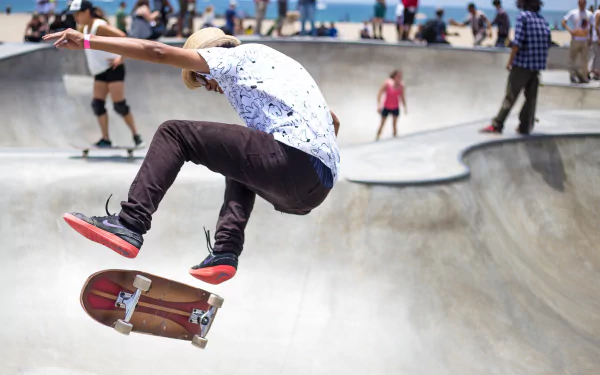 A skateboarder performs a jump at an urban skate park, surrounded by onlookers, capturing the energy and excitement of outdoor sports in this vibrant 4K Ultra HD wallpaper.