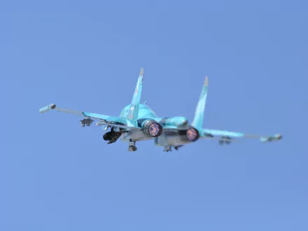 HD desktop wallpaper of a Sukhoi Su-34 military aircraft captured mid-flight against a clear blue sky.