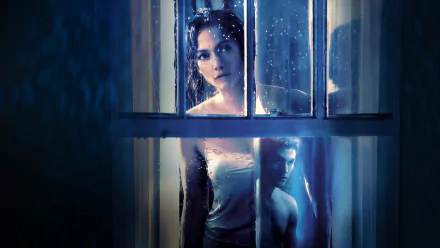 HD desktop wallpaper featuring Jennifer Lopez in a dramatic scene from the movie The Boy Next Door, with a moody blue-toned setting viewed through rain-speckled window panes.