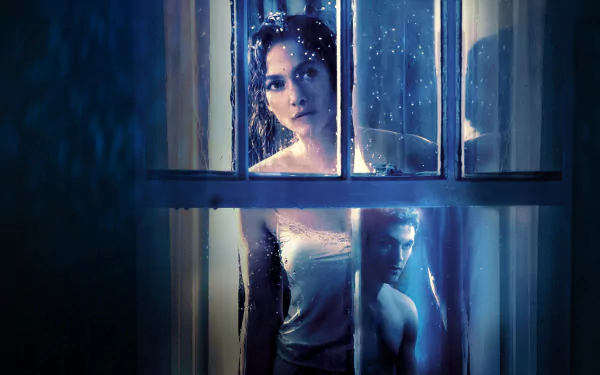 HD desktop wallpaper featuring Jennifer Lopez in a dramatic scene from the movie The Boy Next Door, with a moody blue-toned setting viewed through rain-speckled window panes.