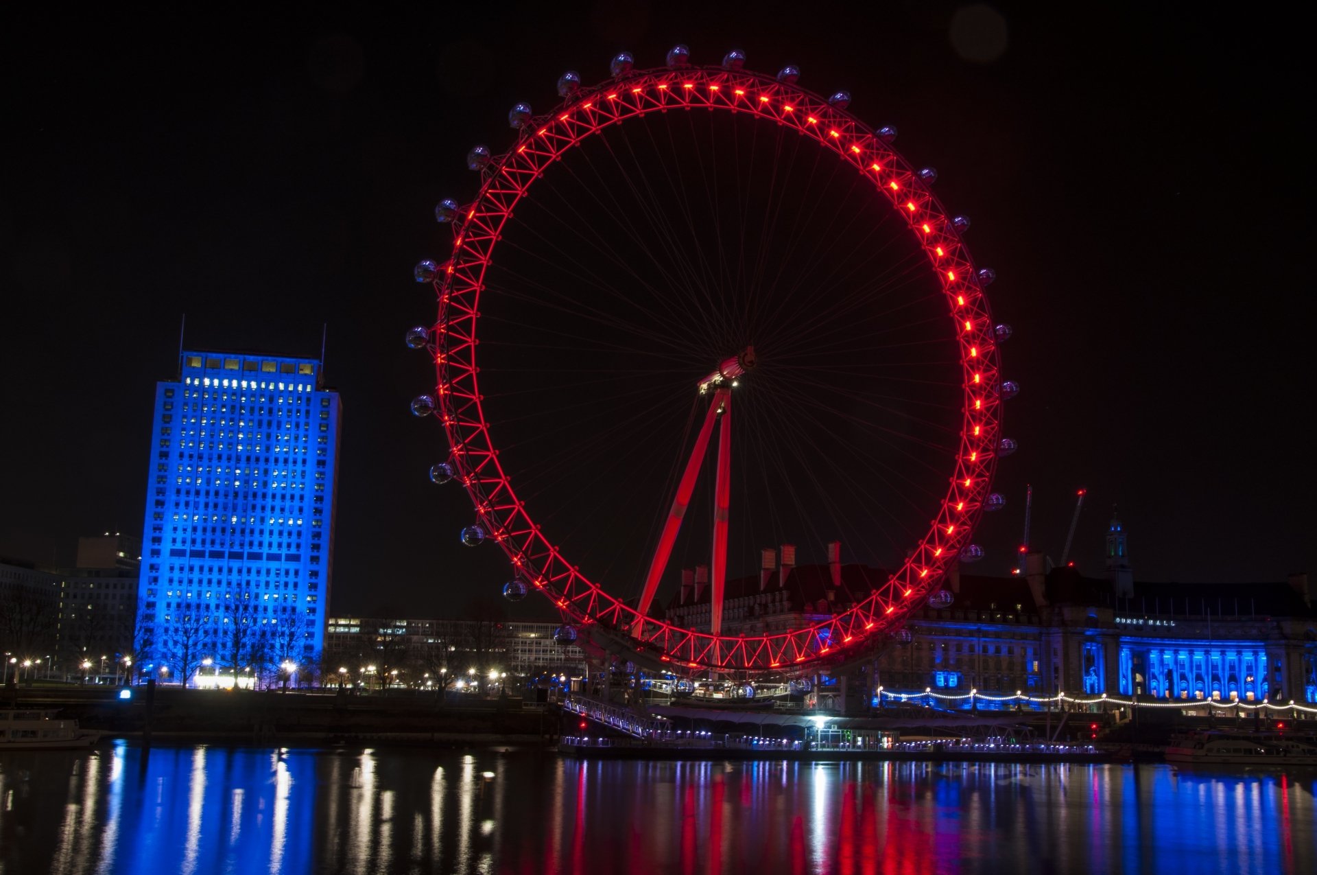 Night view of the illuminated London Eye ferris wheel in England, reflecting vividly on the water, captured in 4K Ultra HD detail as a PC desktop wallpaper.