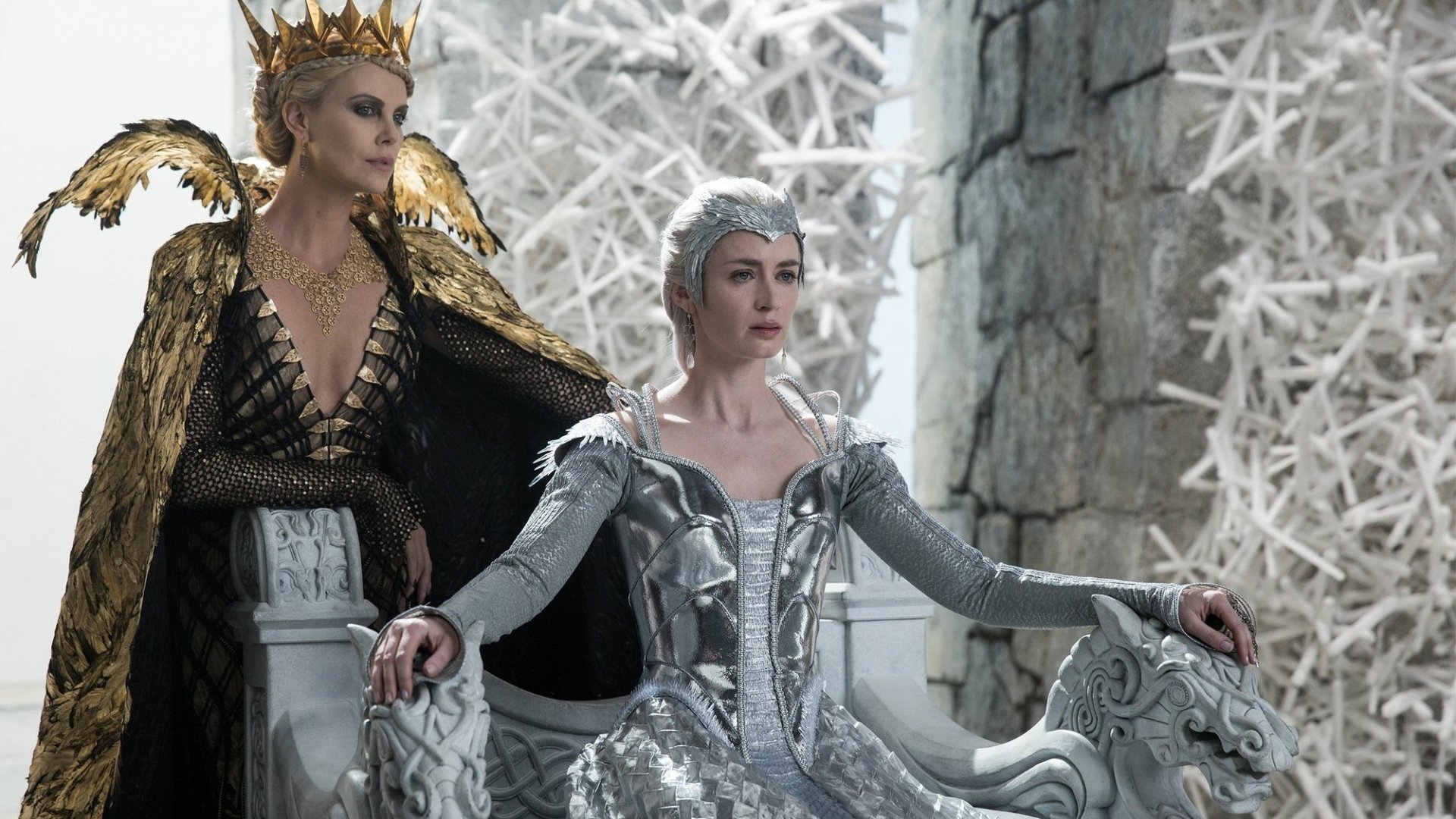 HD desktop wallpaper featuring Charlize Theron and Emily Blunt from the movie The Huntsman: Winter's War in regal, winter-themed costumes.