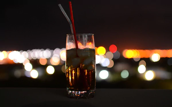 4K Ultra HD PC desktop background of a glass of Coca‑Cola with ice and two straws, a food/drink shot framed against colorful bokeh city lights.