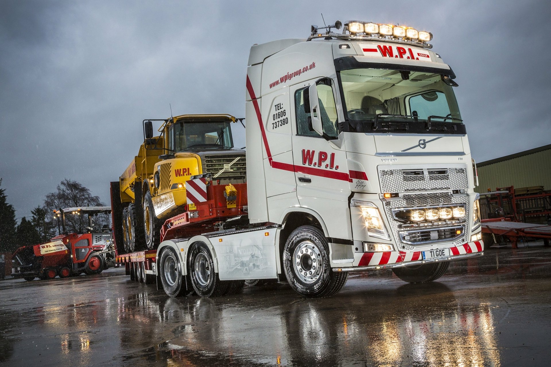HD desktop wallpaper featuring a Volvo truck transporting heavy machinery on a wet surface under a cloudy sky.