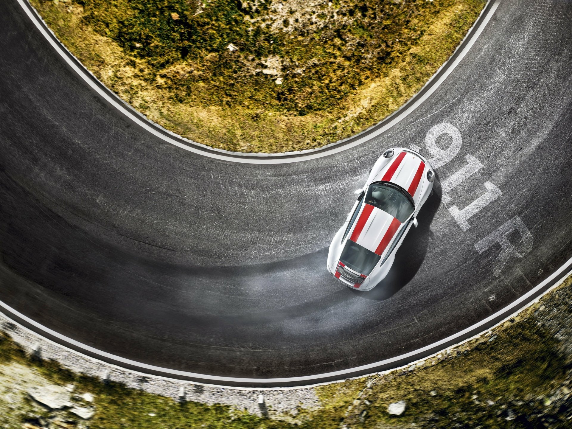 2K Quad HD PC desktop wallpaper: top-down view of a white Porsche 911 vehicle with red racing stripes drifting on a curved mountain road.