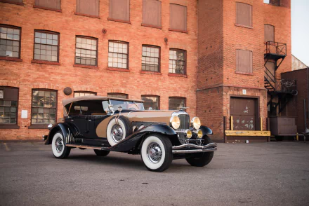 HD PC desktop wallpaper of a classic black Duesenberg Model J parked in front of an industrial brick building.