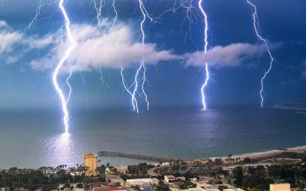 HD PC desktop wallpaper photograph: thunderstorm over a coastal town with multiple lightning bolts striking the ocean beneath dark storm clouds.