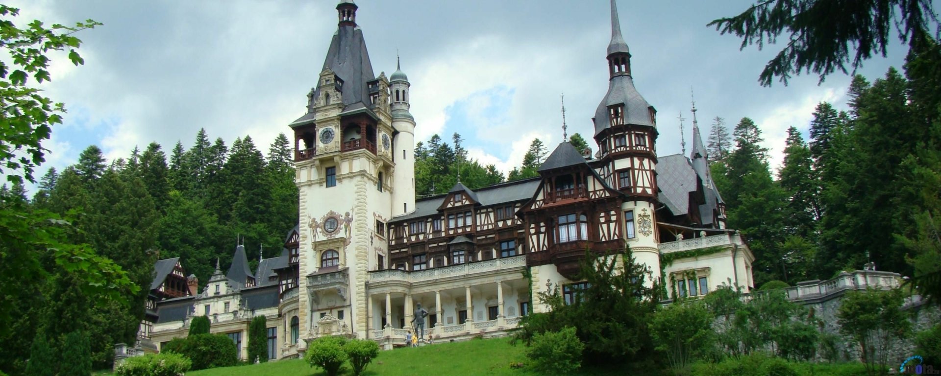 HD desktop wallpaper featuring the man-made architectural beauty of Peles Castle surrounded by lush greenery and an overcast sky.