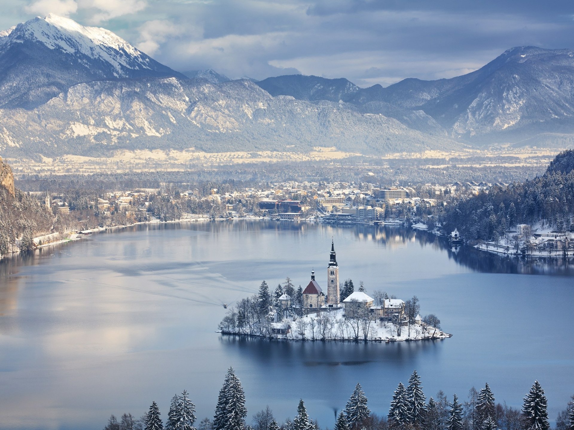 HD desktop wallpaper featuring the Assumption of Mary Church on a snowy island, surrounded by a serene lake and majestic mountains in a religious and peaceful winter landscape.