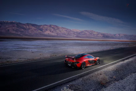 A red McLaren P1 supercar drives on a desert road with mountains in the background, captured as an HD PC desktop wallpaper and background.