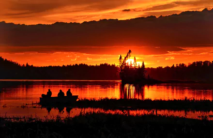 A fishing boat on a lake at sunset, with vibrant orange clouds illuminating the evening sky in this 4K Ultra HD desktop wallpaper.