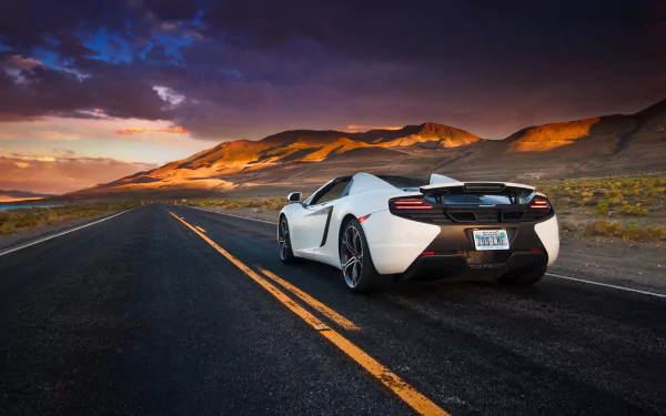 White McLaren MP4-12C Spider supercar drives on an open road at sunset, set against a scenic mountainous desert landscape in this HD desktop wallpaper.