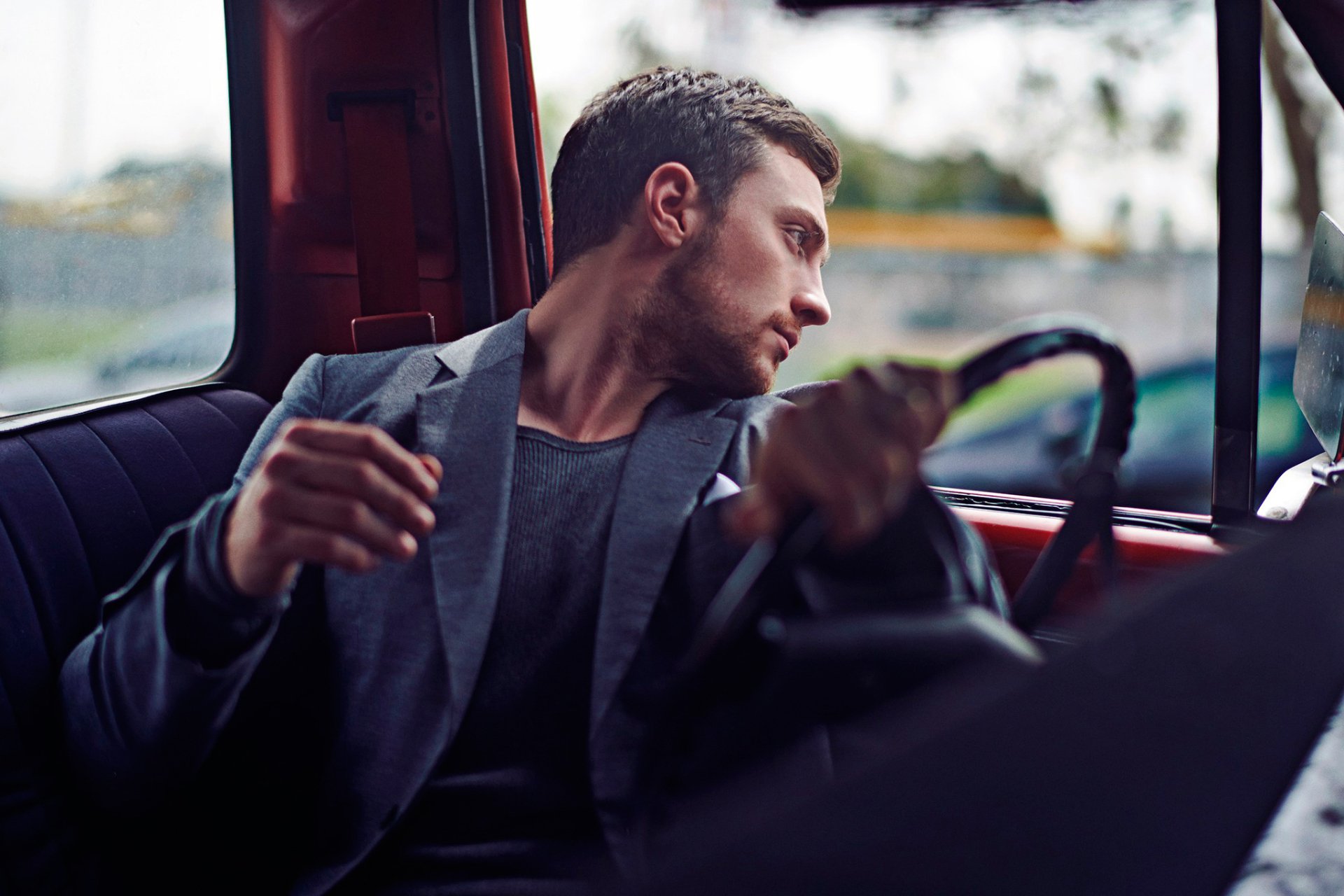 HD desktop wallpaper featuring celebrity Aaron Taylor-Johnson seated in a car, gazing out the window with a contemplative expression.