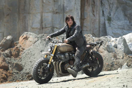 HD desktop wallpaper featuring Norman Reedus as Daryl Dixon from the TV show The Walking Dead. He is sitting on a motorcycle in a rugged, rocky landscape.