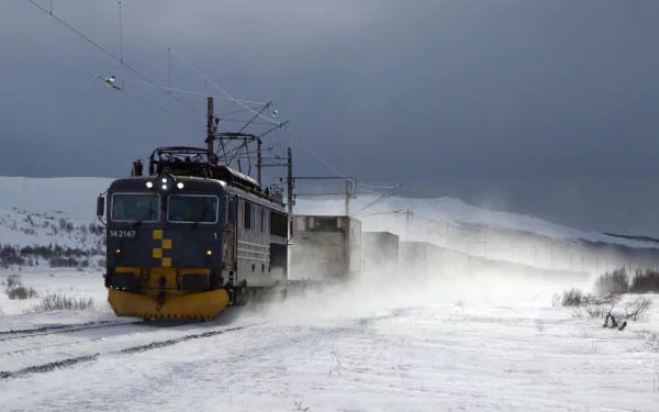 A powerful train travels through a snowy landscape, creating a cloud of snow as it moves along the tracks under a moody sky. A striking HD desktop wallpaper for enthusiasts of vehicles and trains.
