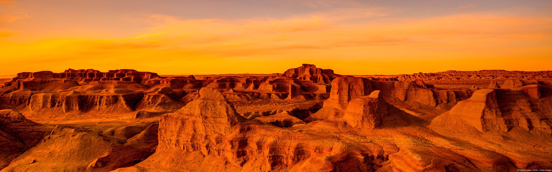HD PC desktop wallpaper: golden sunset over the Gobi Desert, rugged sandstone formations and rolling dunes bathed in warm orange light, a serene nature scene.