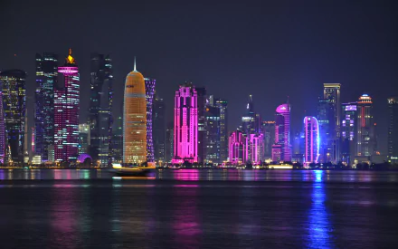 HD wallpaper of Doha, Qatar at night, showcasing the illuminated city skyline with colorful skyscrapers reflecting on the water.