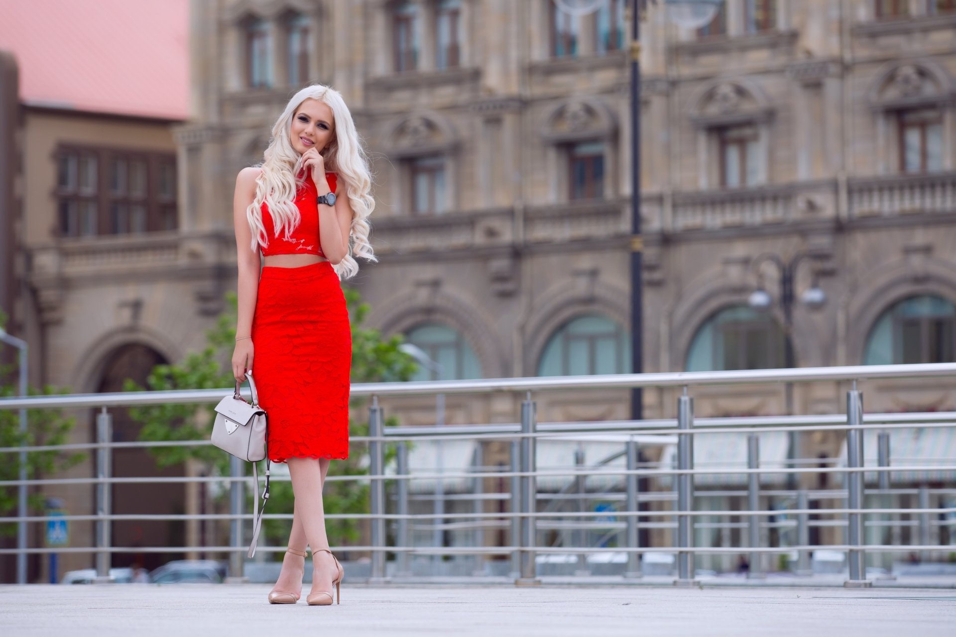 Blonde woman in a red dress poses confidently against a historic building backdrop, captured in stunning 4K Ultra HD for a PC desktop wallpaper.