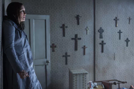 Vera Farmiga in The Conjuring 2, standing against a wall covered with crucifixes. The image is a HD wallpaper and background from the movie.