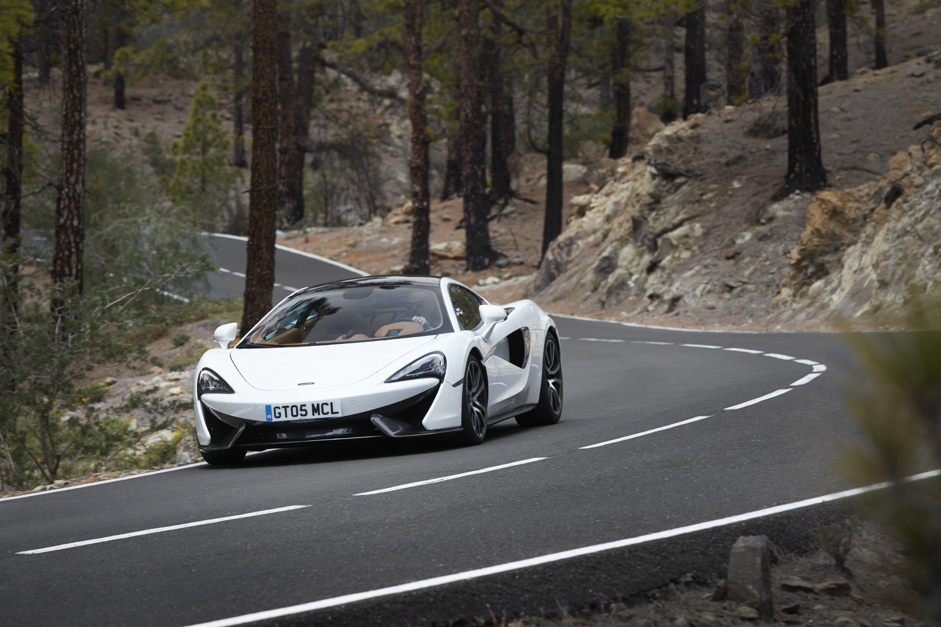 White McLaren 570GT supercar driving on a winding mountain road, captured in 4K Ultra HD as a PC desktop wallpaper and background.