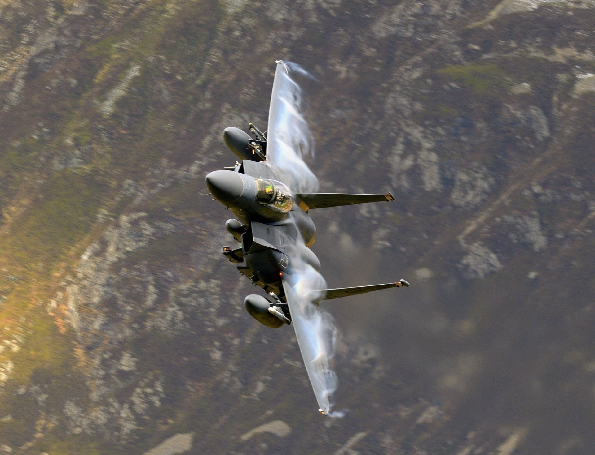 A McDonnell Douglas F-15 Eagle jet fighter warplane in flight against a mountainous backdrop, captured in high definition for a dynamic desktop wallpaper.