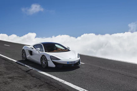 White McLaren 570GT supercar parked on an open mountain road under a bright blue sky with clouds, showcased in 4K Ultra HD as a desktop wallpaper.