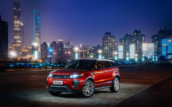 A red Range Rover Evoque SUV by Land Rover is parked against a vibrant city skyline at night, captured in stunning 4K Ultra HD for PC desktop wallpaper.