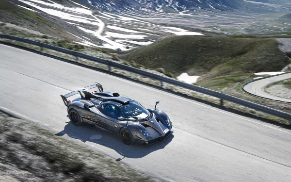 Black Pagani Zonda supercar driving on a winding mountain road, captured in 4K Ultra HD for a dynamic PC desktop wallpaper.